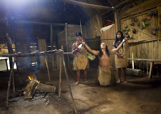 3 Indigenous peoples are shown performing various musical instruments in a dimly lit room (Palenque) on a visit to the Maleku Reserve in Costa Rica.