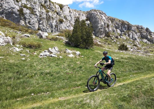 A biker cycled along a grassy path with limestone massifs in the background. This is in the French Alps on a sunny day on a sustainable cycling tour.