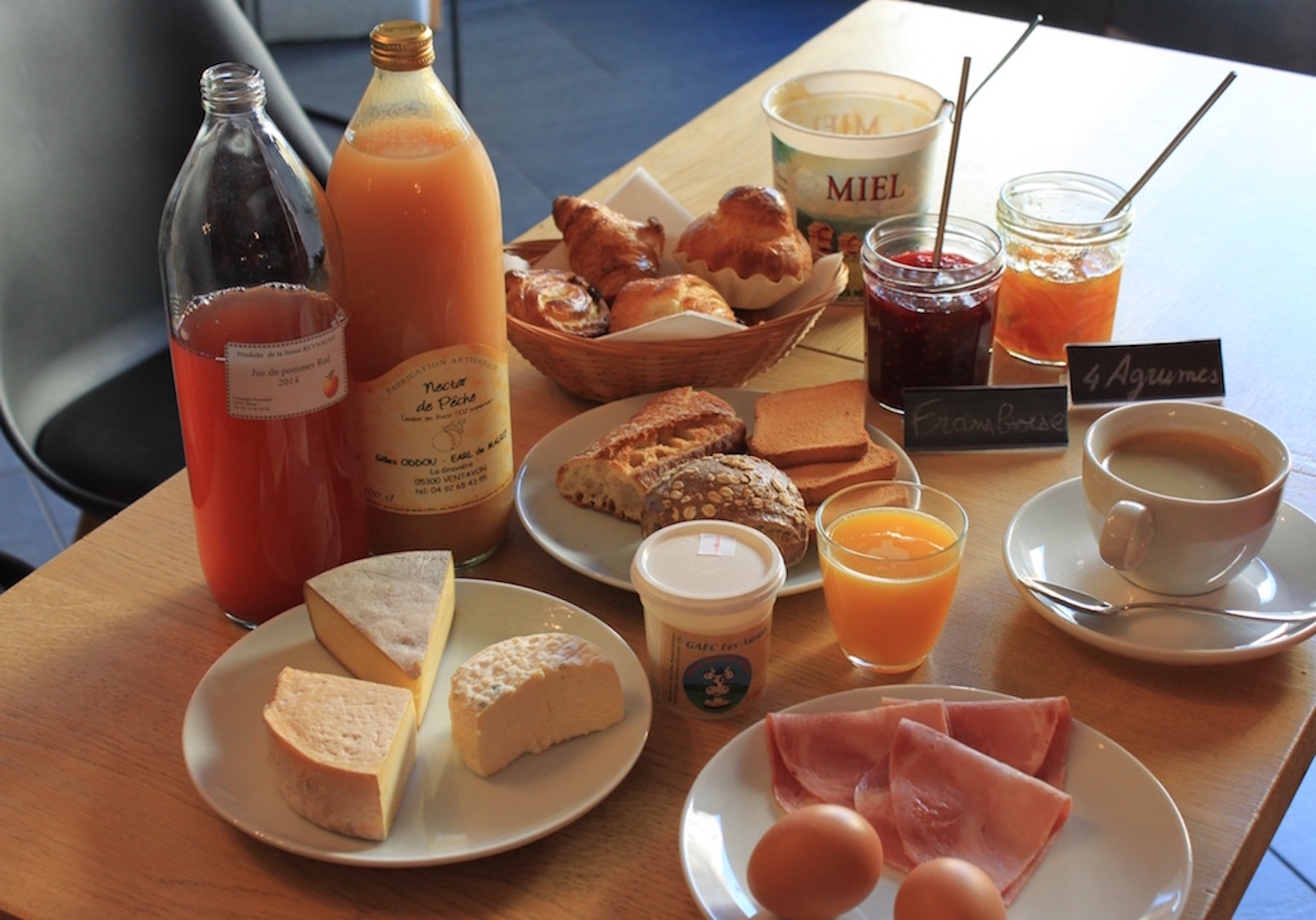 A classic French breakfast from a bed & breakfast hotel is shown with bread, cheese, juice, and other regional products.