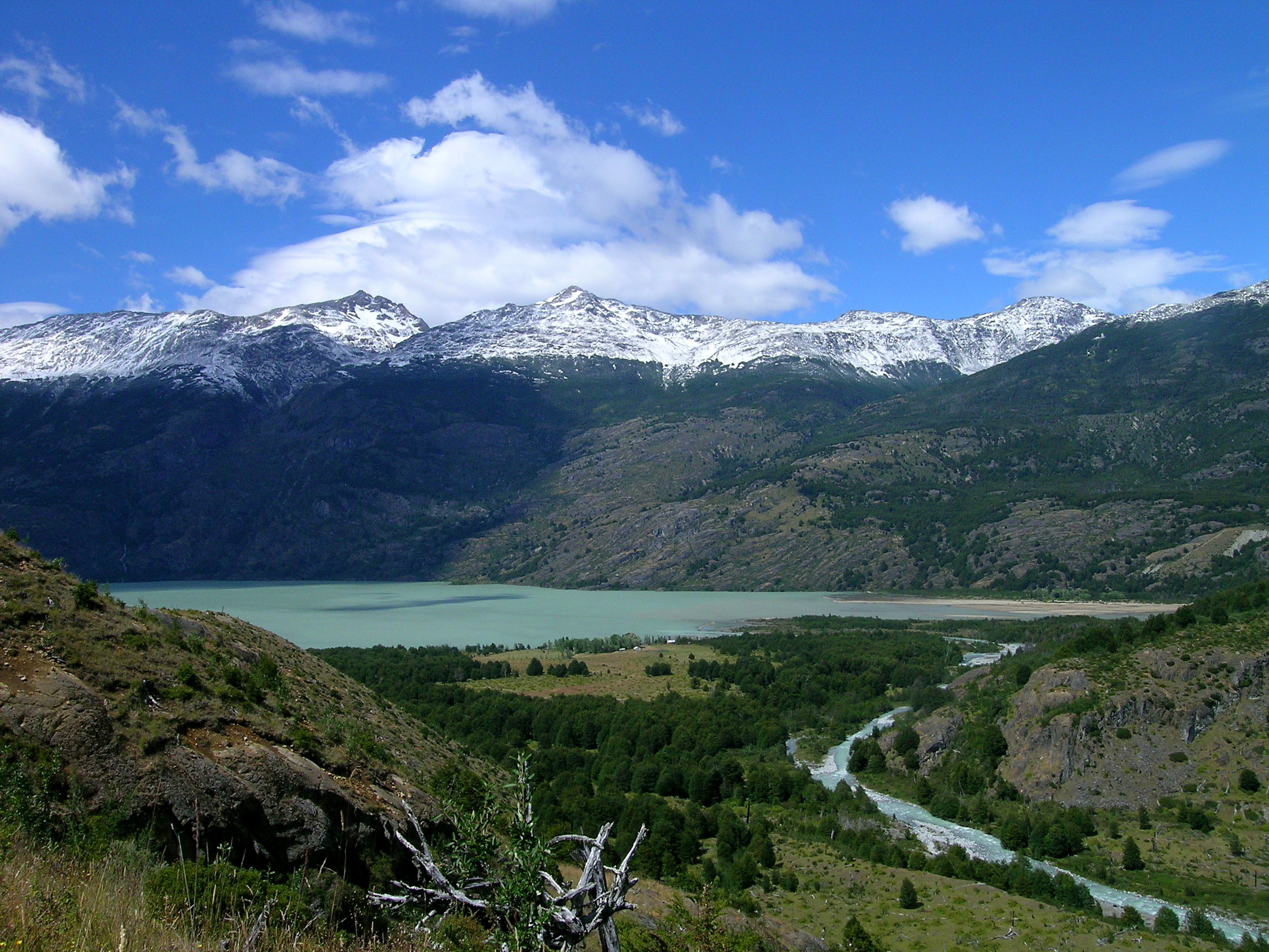 A teal alpine lake sits in front of snow capped mountains along the El Gaucho Way in Chilean Patagonia.