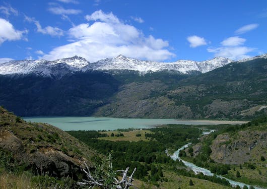 A teal alpine lake sits in front of snow capped mountains along the El Gaucho Way in Chilean Patagonia.