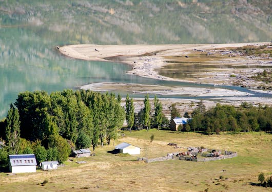 The varied landscape of the wild wilderness of Chilean Patagonia is shown, with meadows, dirt, streams, trees, and a hillside. This is during a responsible supported trek along the El Gaucho Way.