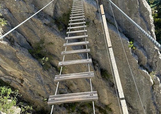 A wooden suspension bridge is shown along a Via Ferrata route in the French Alps.