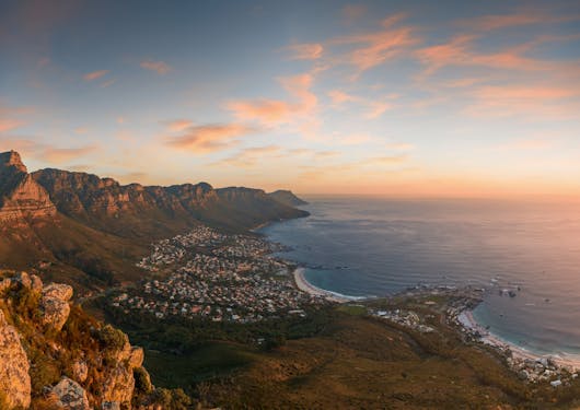 A view of Table Mountain in South Africa is shown to the left of the ocean during an ethereal orangey-pink sunset.