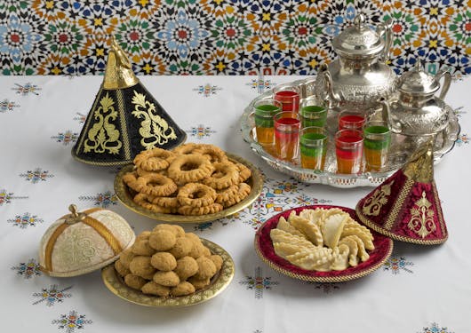 Traditional Moroccan cookies and snacks are presented in trays next to a tea pot with tea glasses.