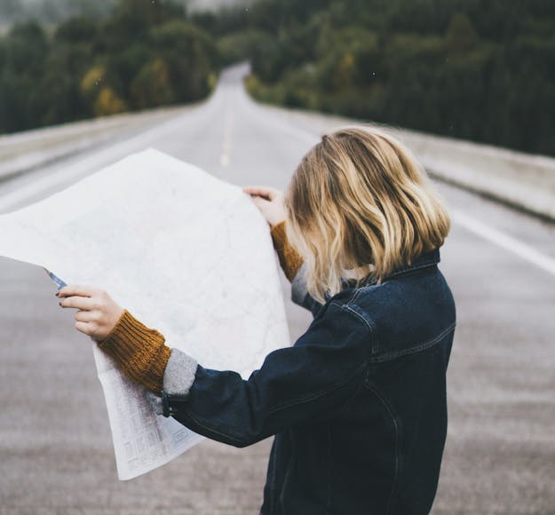 A student looks over a map, questioning where to go next, while standing on an open road.