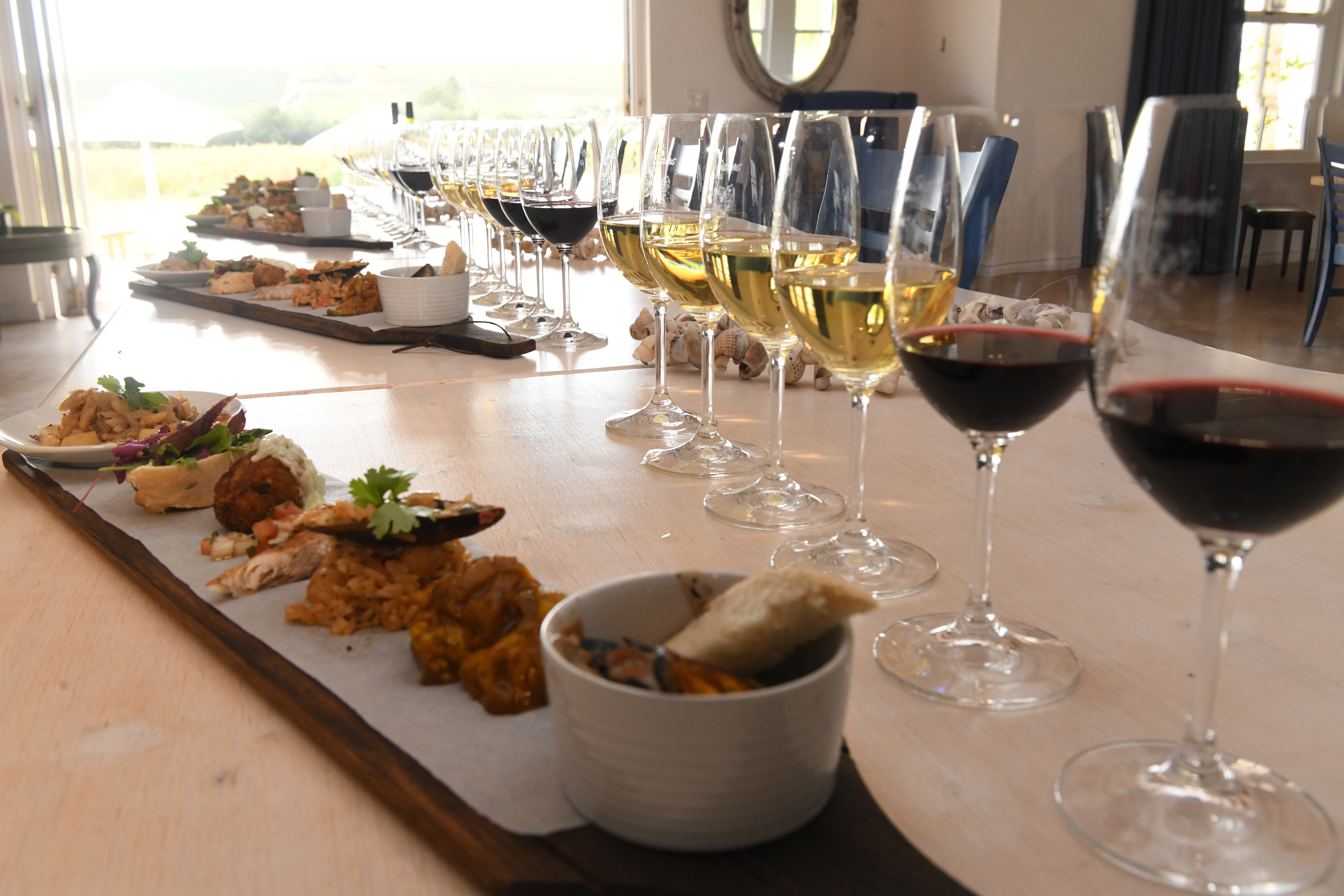 Wine blending in the Cape Winelands; many glasses are set out in a row with whites and reds and snacks in front of them for a tasting and pairing session.