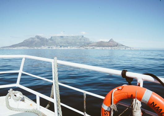 View from Robben Island towards Table Mountain from aboard a boat, with an orange life ring in the foreground tied to white boat rails.