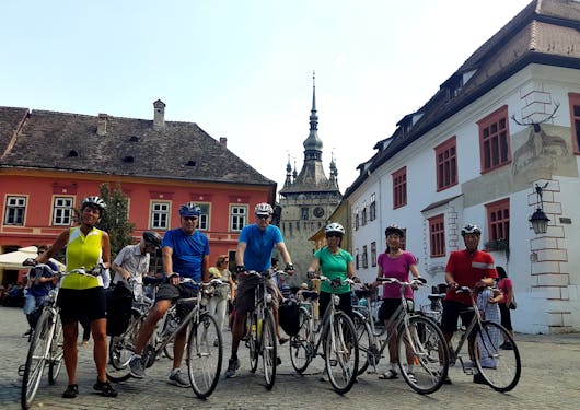 A group of bikers stand in a town square straddling their bikes in a rural town in Romania on a guided cycling tour.