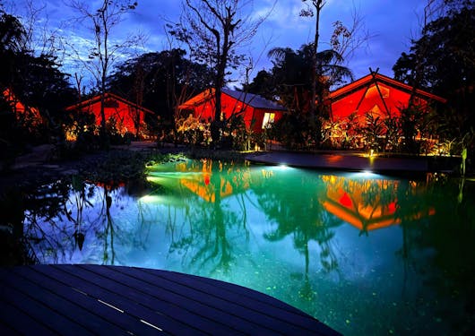 Glamping in Costa Rica is shown at night, with soft red lighting reflecting onto a pool at dusk.