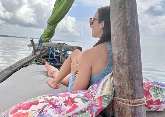 An adult female traveler sits with her back against a pole aboard a dhow as it sails the Kenyan coast.