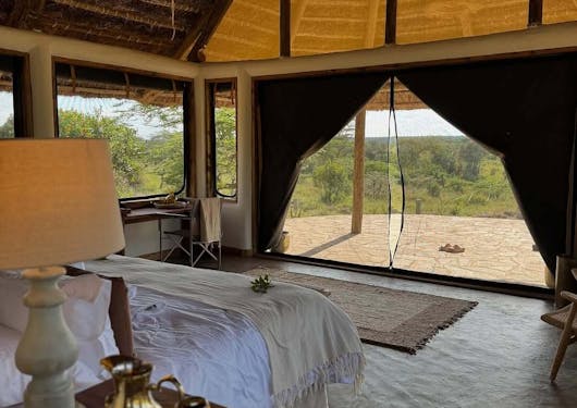 Accommodation at a safari lodge in Kenya shows a bed with a view of the grassy savannah.