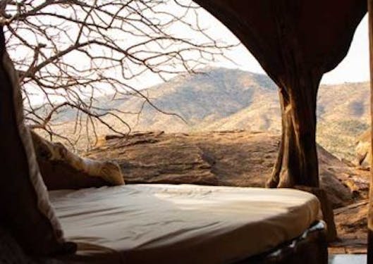 A lodge room is shown in Kenya with the view from the bed out to the savannah.