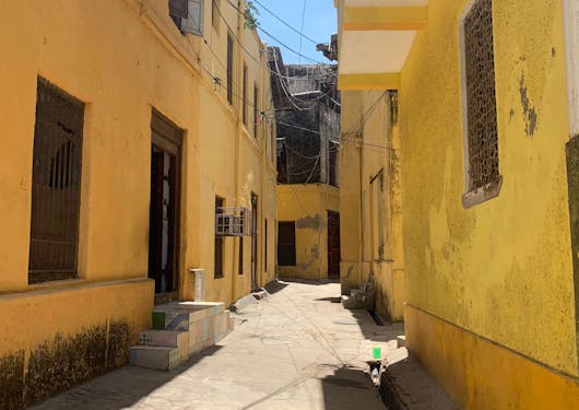 Yellow buildings of old town Mombasa in Kenya are shown lining an empty street on a sunny day.