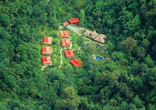 An eco lodge in Costa Rica is shown from an aerial view, nestled amongst a dense rainforest.