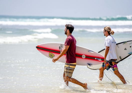Two young adult male surfers head out ot the ocean with their surfboards in Sri Lanka.