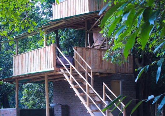 A treehouse cabin in the forested woods of Sri Lanka is shown, with stairs leading up to an open air sleeping areal.