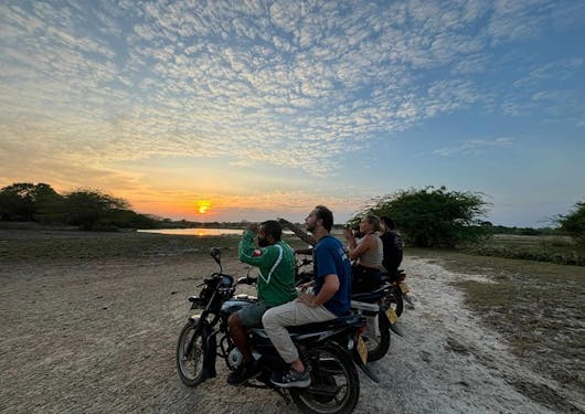 A group of travelers with their expert guides on a motor bike safari in Sri Lanka, stopping at sunset.