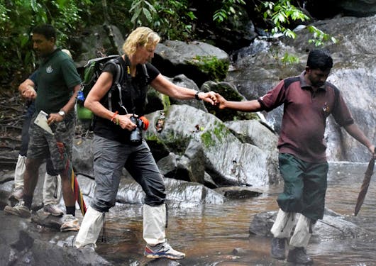 An adult woman is guided across a stream in Sri Lanka by an expert local guide while wearing gaiters and leech socks.
