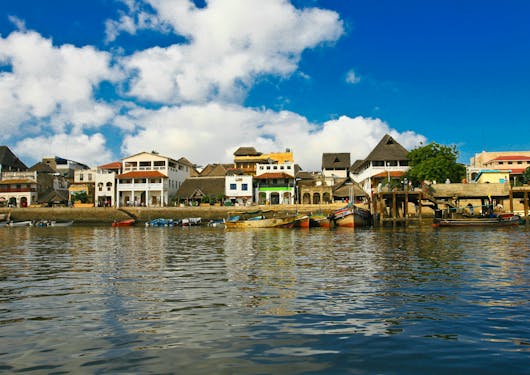 The coastline of Lamu, a car-free island in Kenya, is shown with colorful houses along the water.