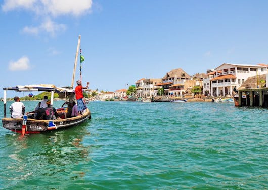 A small boat sails on turquoise waters off the coast of Lamu, Kenya.