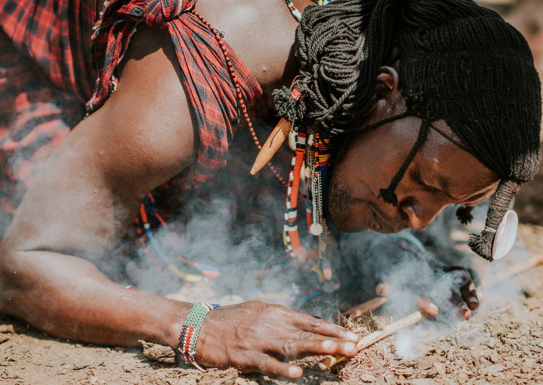 A local Kenyan man kneels to the ground as he lights a fire.