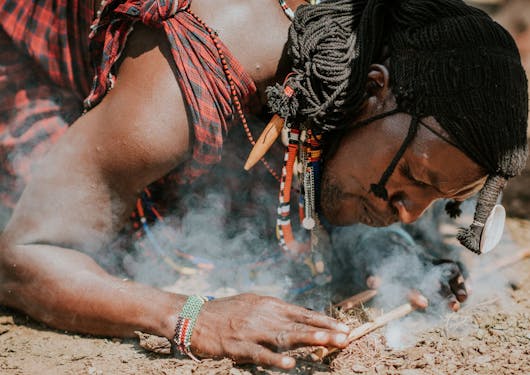 A local Kenyan man kneels to the ground as he lights a fire.