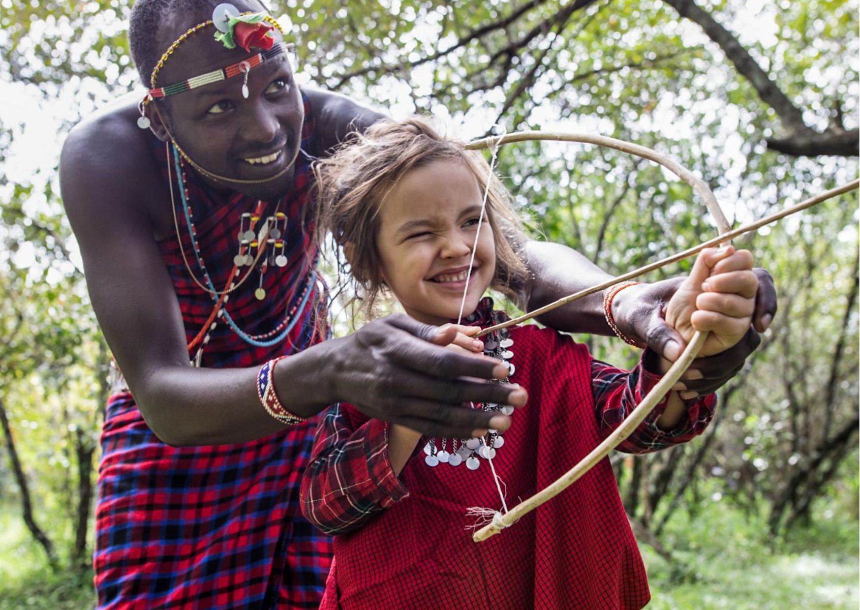 A local Kenyan man shows a young girl how to shoot a bow and arrow.