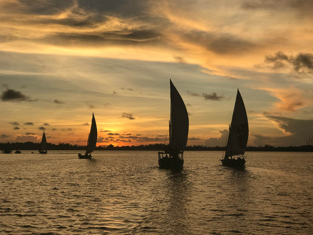 Dhows (boats) are shown at sunset off the coast of Lamu, Kenya.