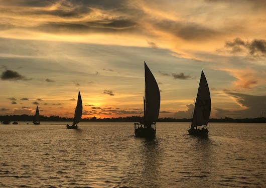 Dhows (boats) are shown at sunset off the coast of Lamu, Kenya.