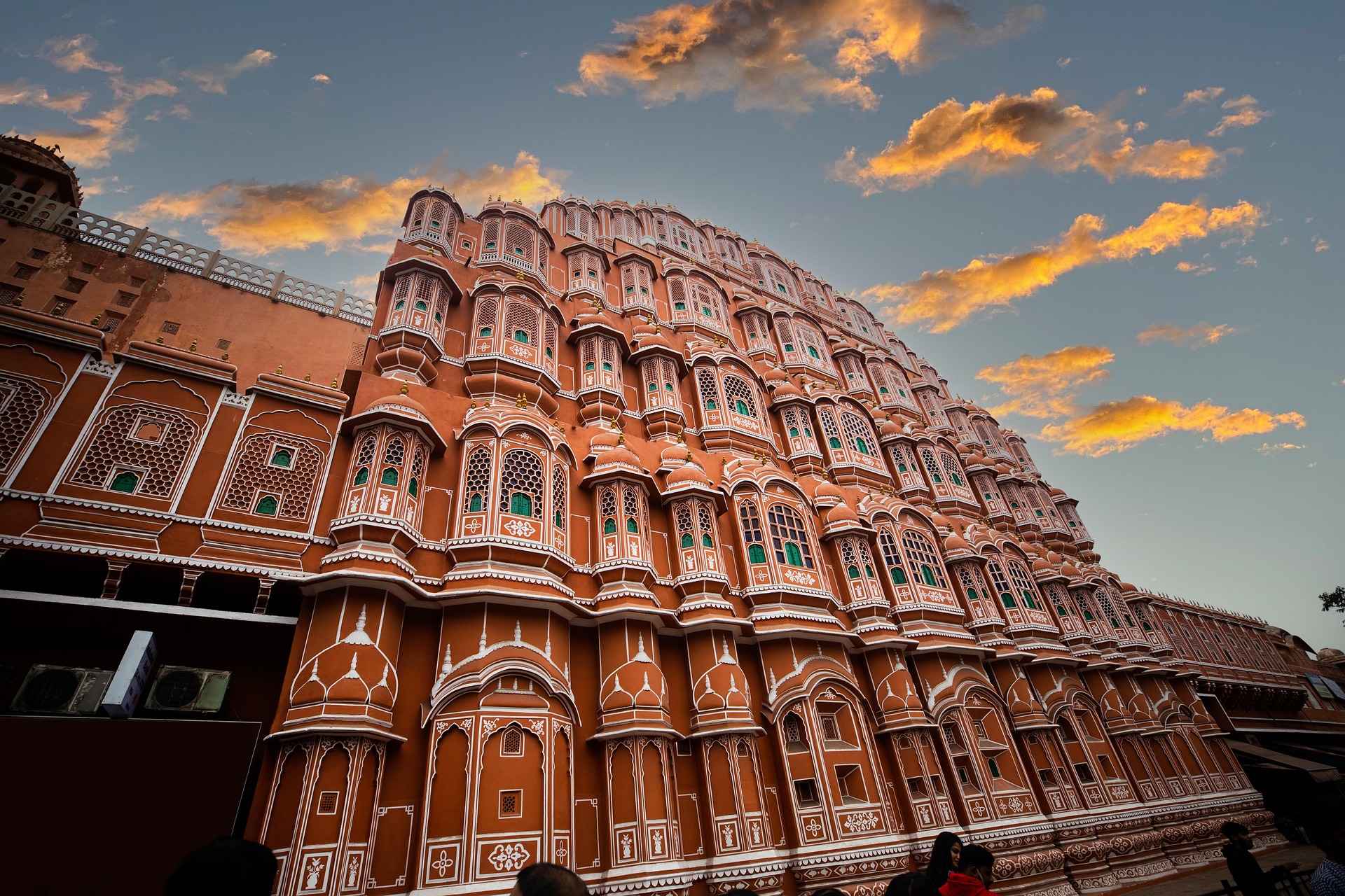 The Hawa Mahal in Jaipur, India, is shown at sunset with hues of its red and pink sandstone and ornate architecture. 