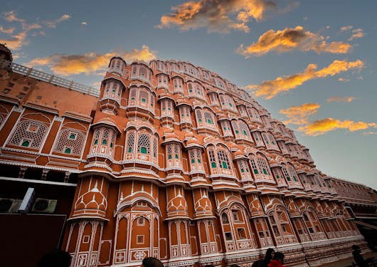 The Hawa Mahal in Jaipur, India, is shown at sunset with hues of its red and pink sandstone and ornate architecture.
