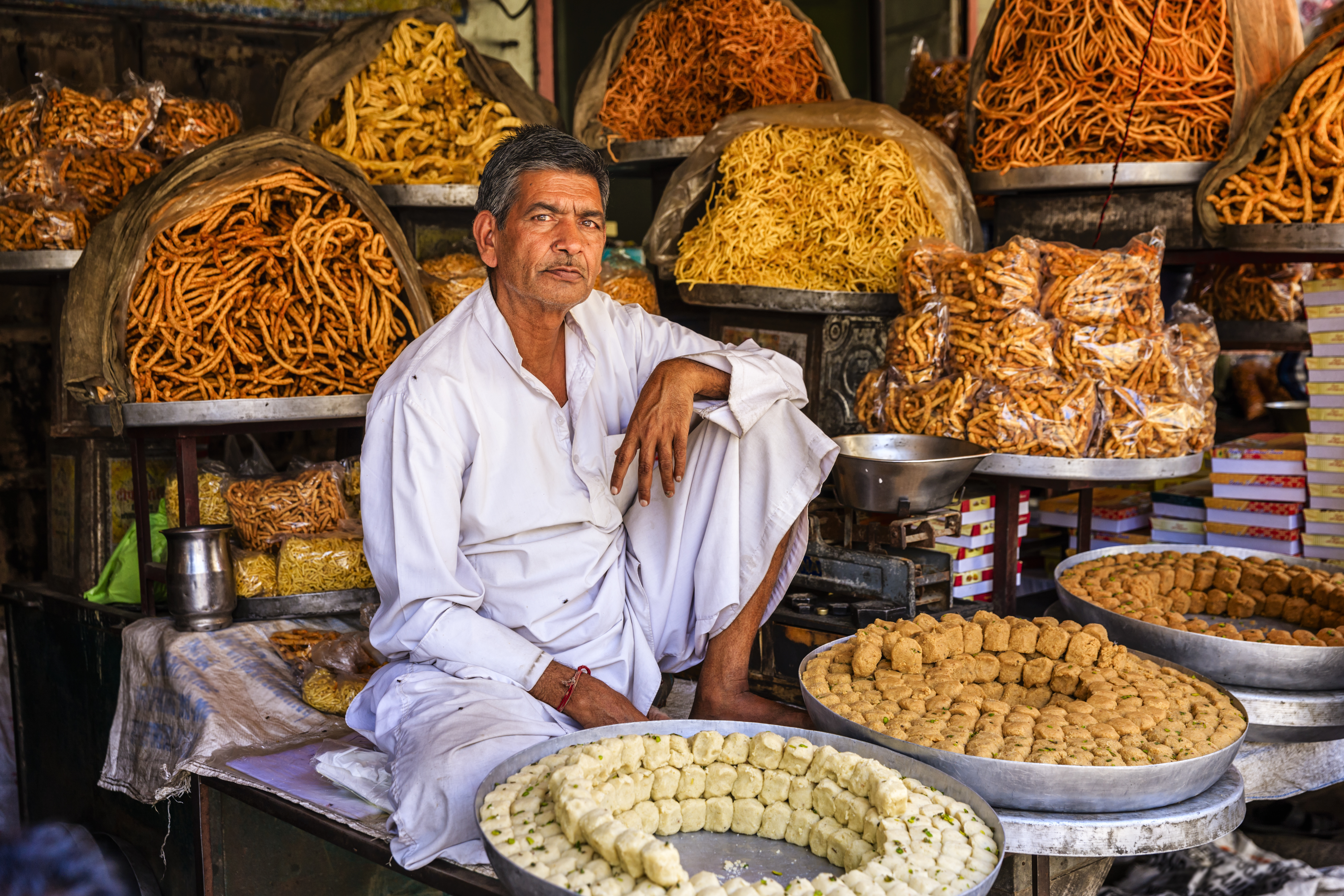 A market stall vendor stands with his colorful orange and yellow-hued food in Jaipur, India.