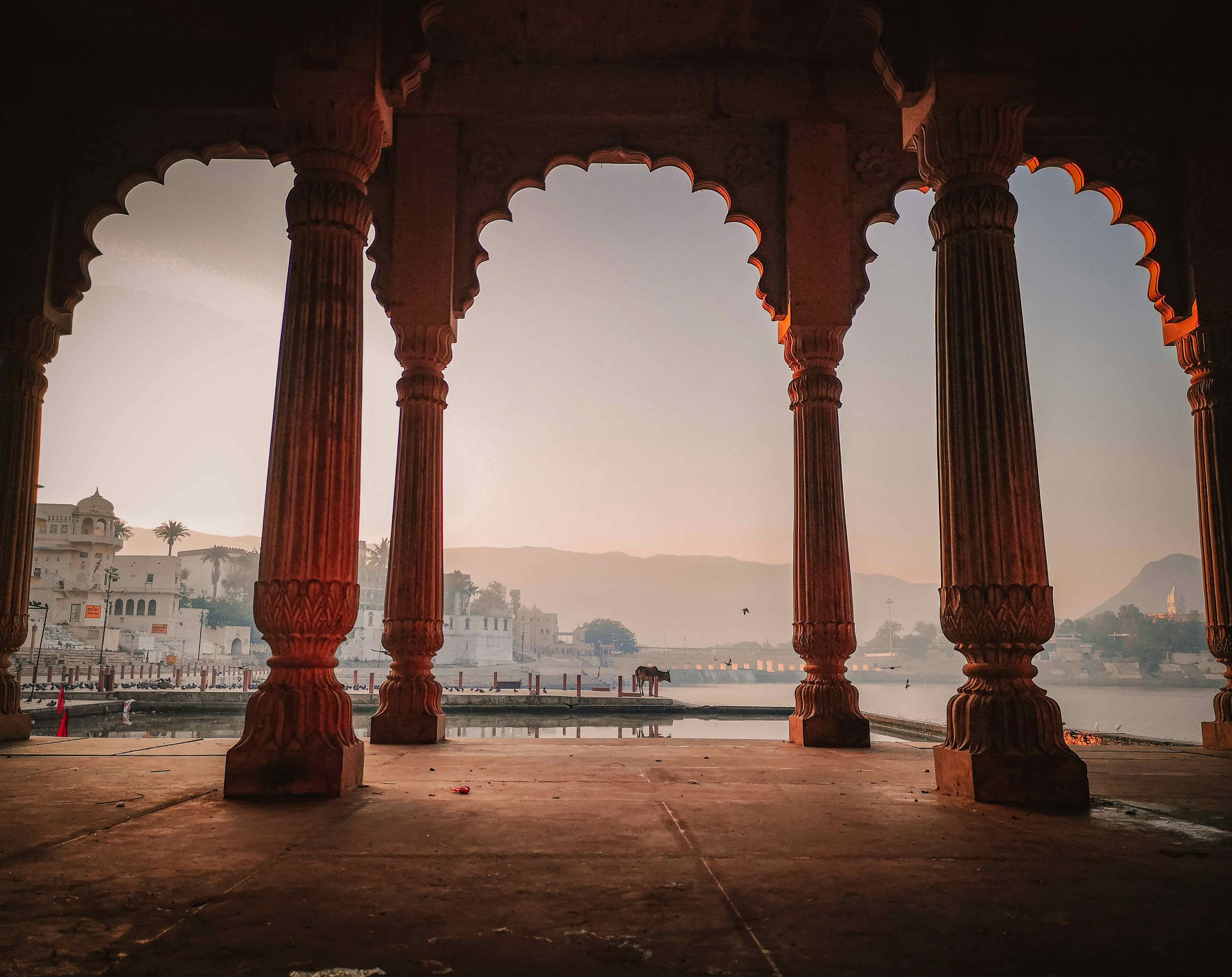 A few through beautiful arches in Agra, India is shown with the city at dusk in the background.