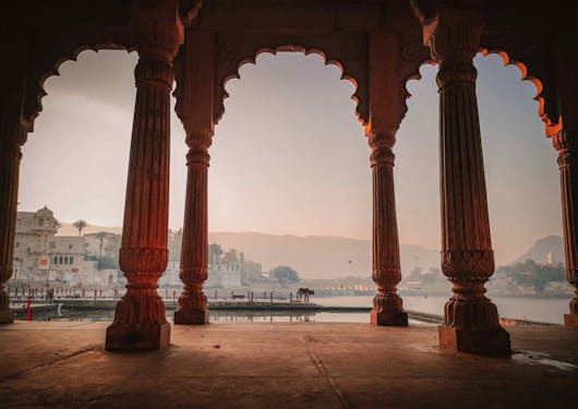 A few through beautiful arches in Agra, India is shown with the city at dusk in the background.