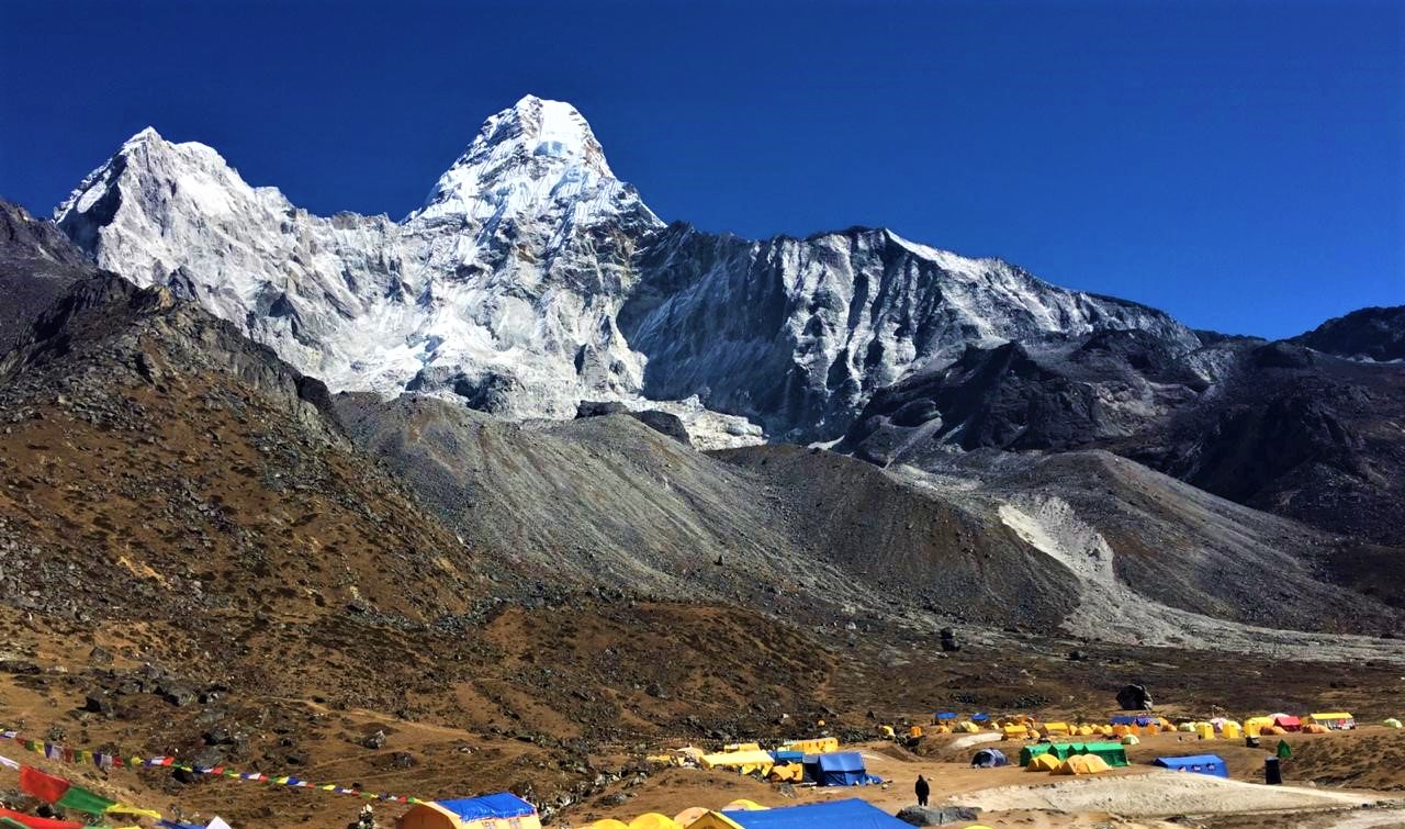 A camp along the Amadablam Base Camp trail is shown at the foot of towering mountains.