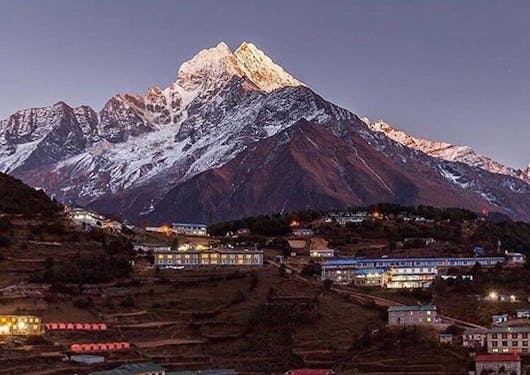 A town lit up at night is shown in front of a towering mountain in the Himalayas.