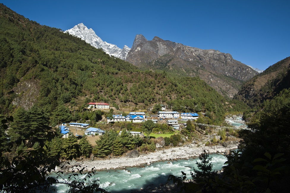 A green river rushes past a small town nestled in the Himalayas.