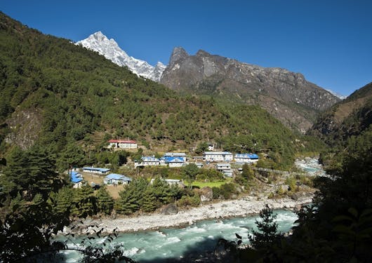 A green river rushes past a small town nestled in the Himalayas.
