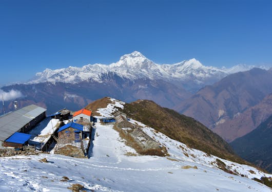 A snowy clearing with some small buildings on it is perched high and overlooking the mountains.