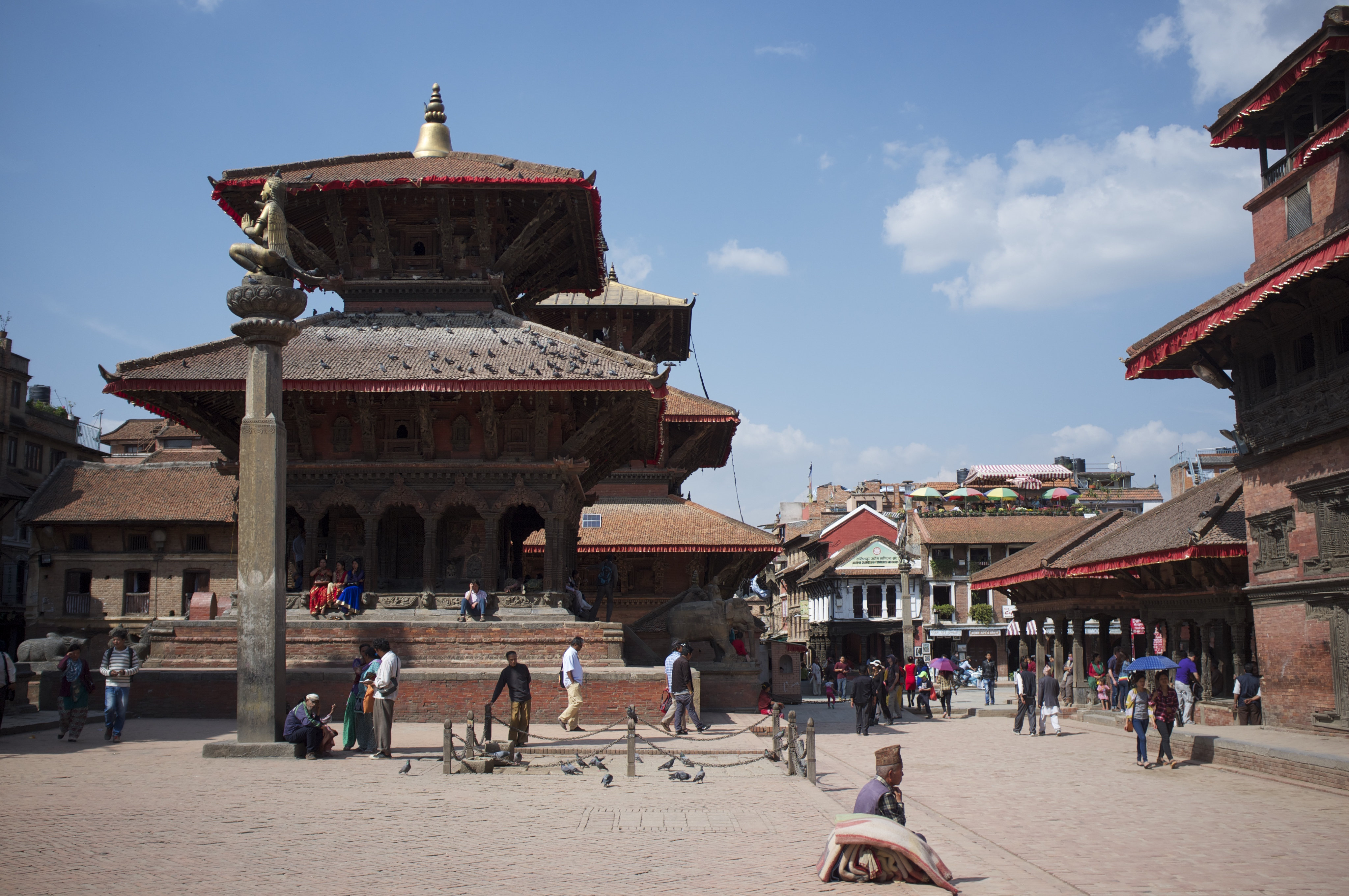 Patan Durbar Square in Kathmandu, India, is shown with people walking around the buildings.