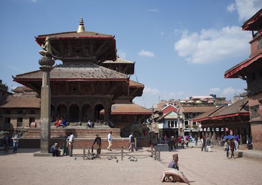 Patan Durbar Square in Kathmandu, India, is shown with people walking around the buildings.
