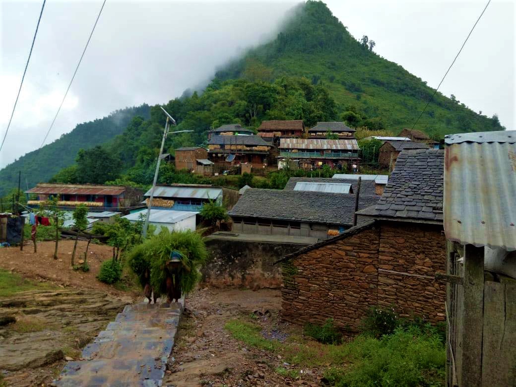 Ramkot Village in India, with a path leading into the village and a pointy green peak in the background.