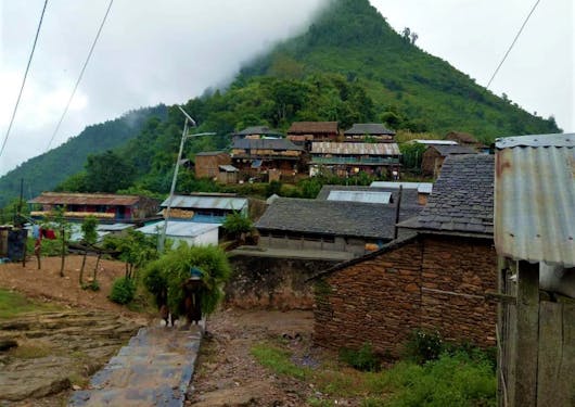 Ramkot Village in India, with a path leading into the village and a pointy green peak in the background.