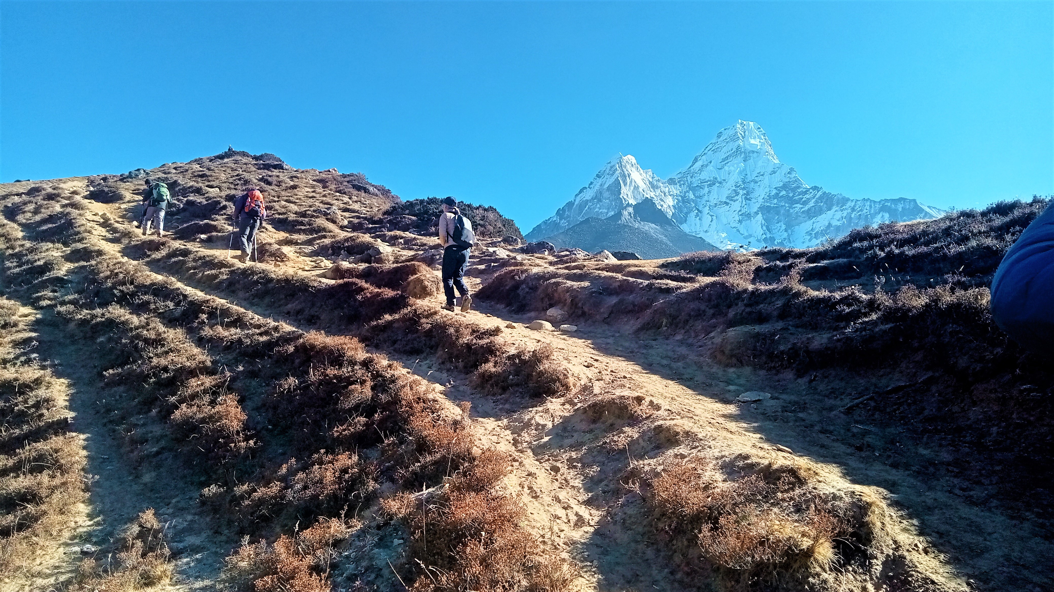 A view of trekkers on the trail along the Everest Base Camp trek with Mount Everest in the background.
