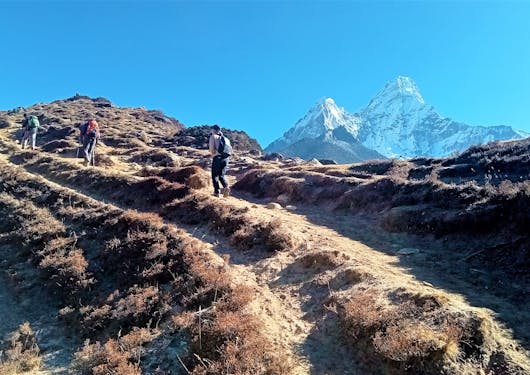 A view of trekkers on the trail along the Everest Base Camp trek with Mount Everest in the background.