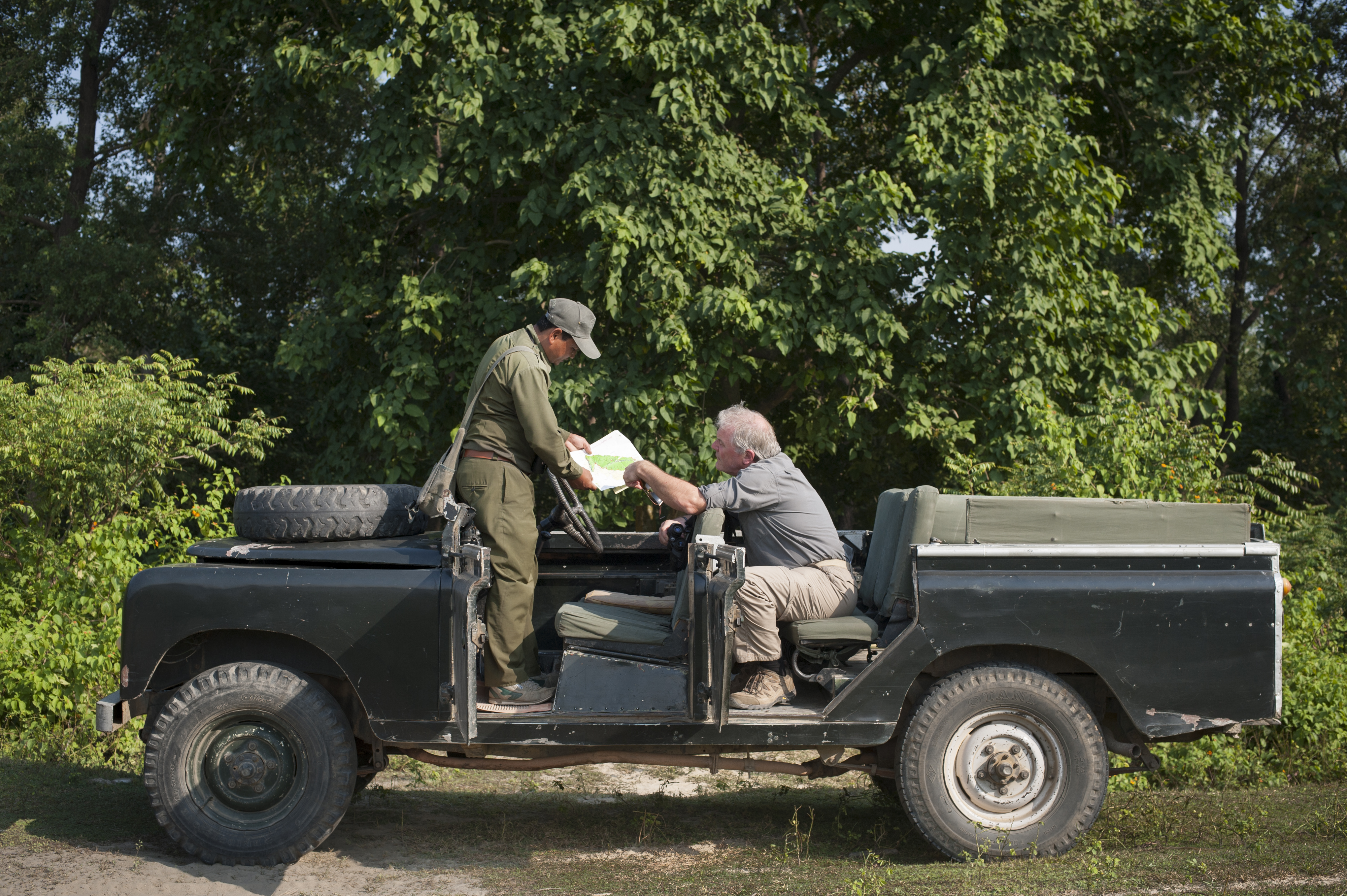 A traveler and guide stop in the safari jeep to look at a map.