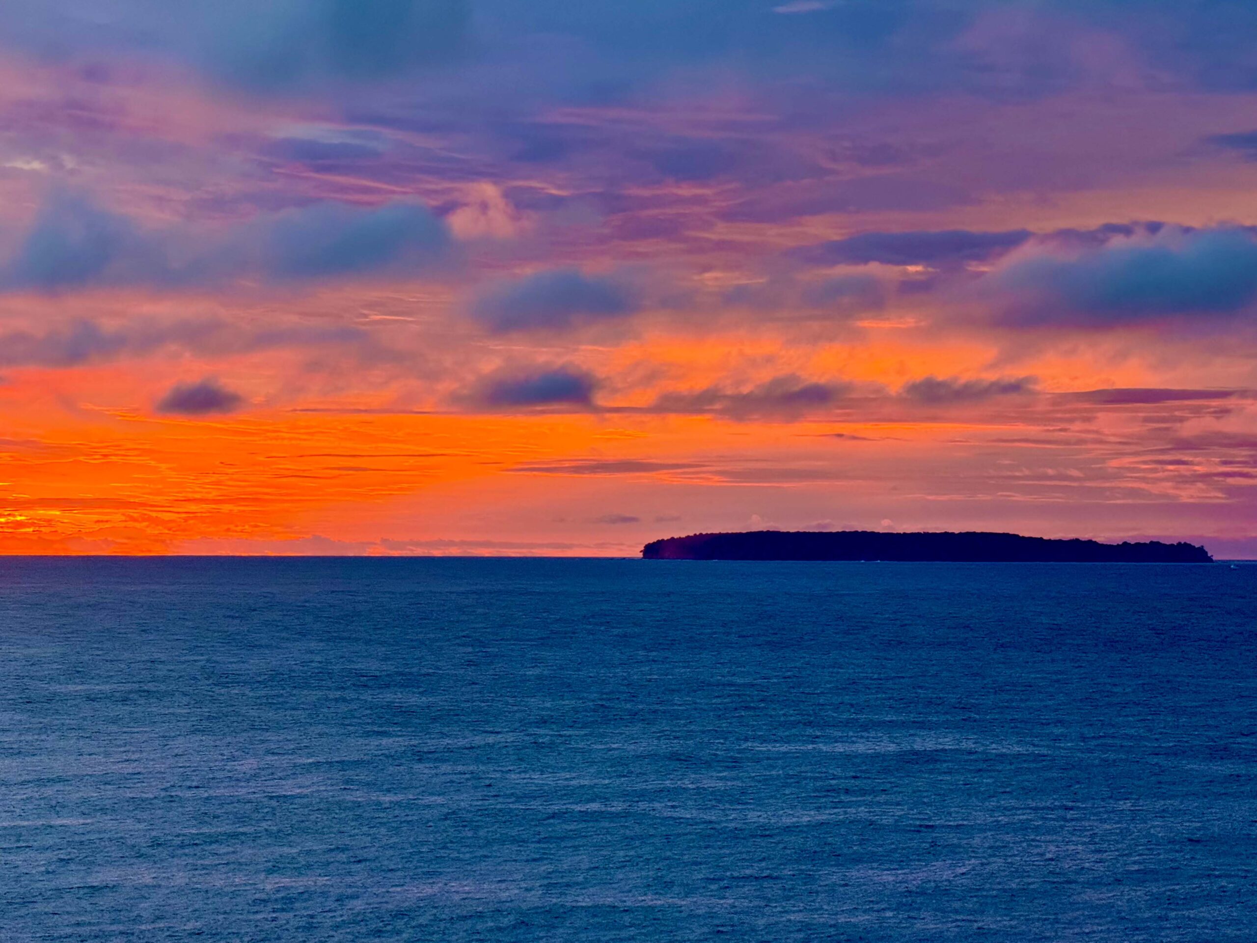 Sunset in Costa Rica, with a red orange sky over blue water.