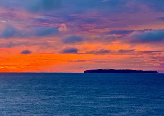 Sunset in Costa Rica, with a red orange sky over blue water.