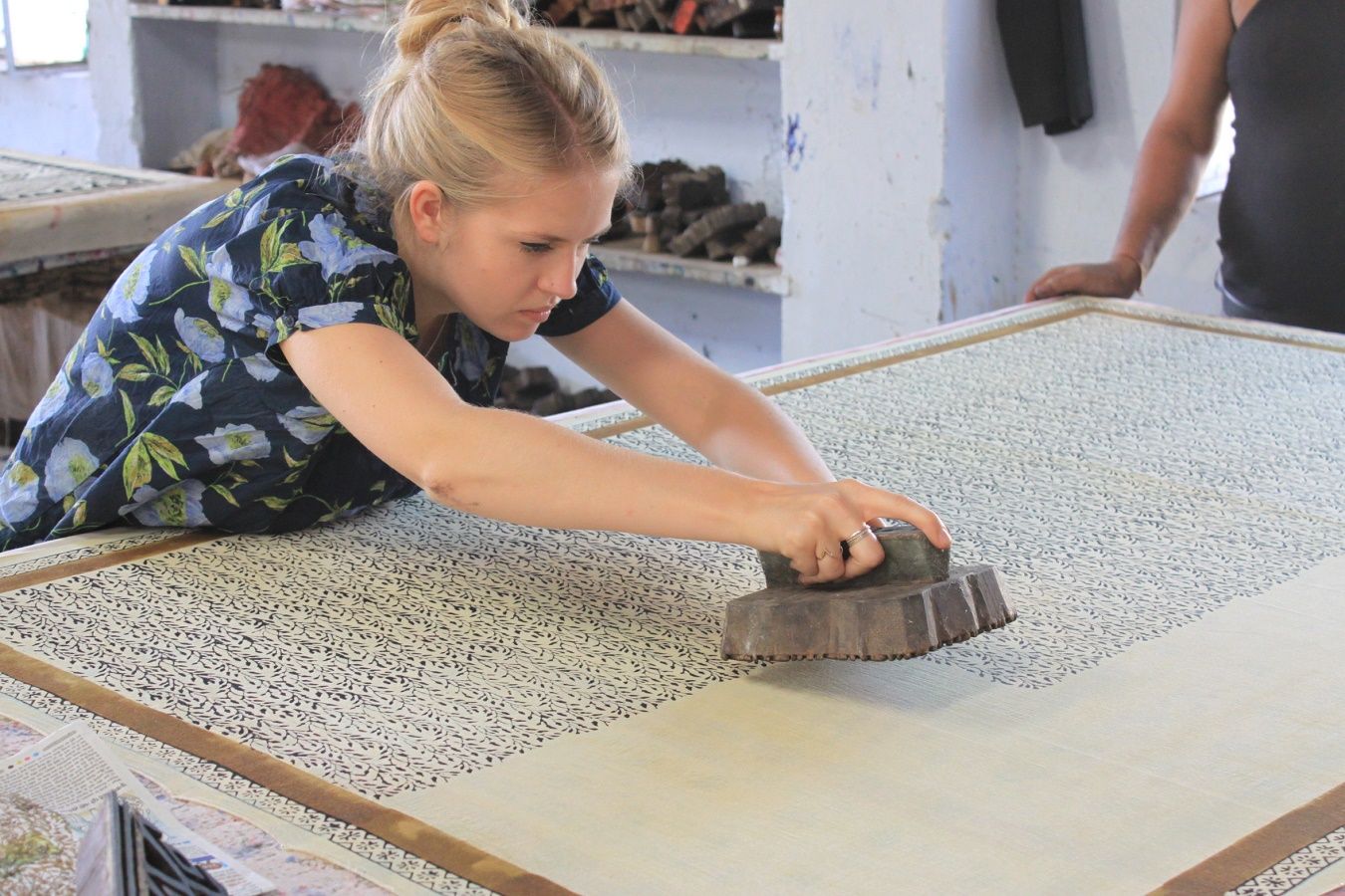 An adult female white traveler uses a block printer at an artisan visit in India.